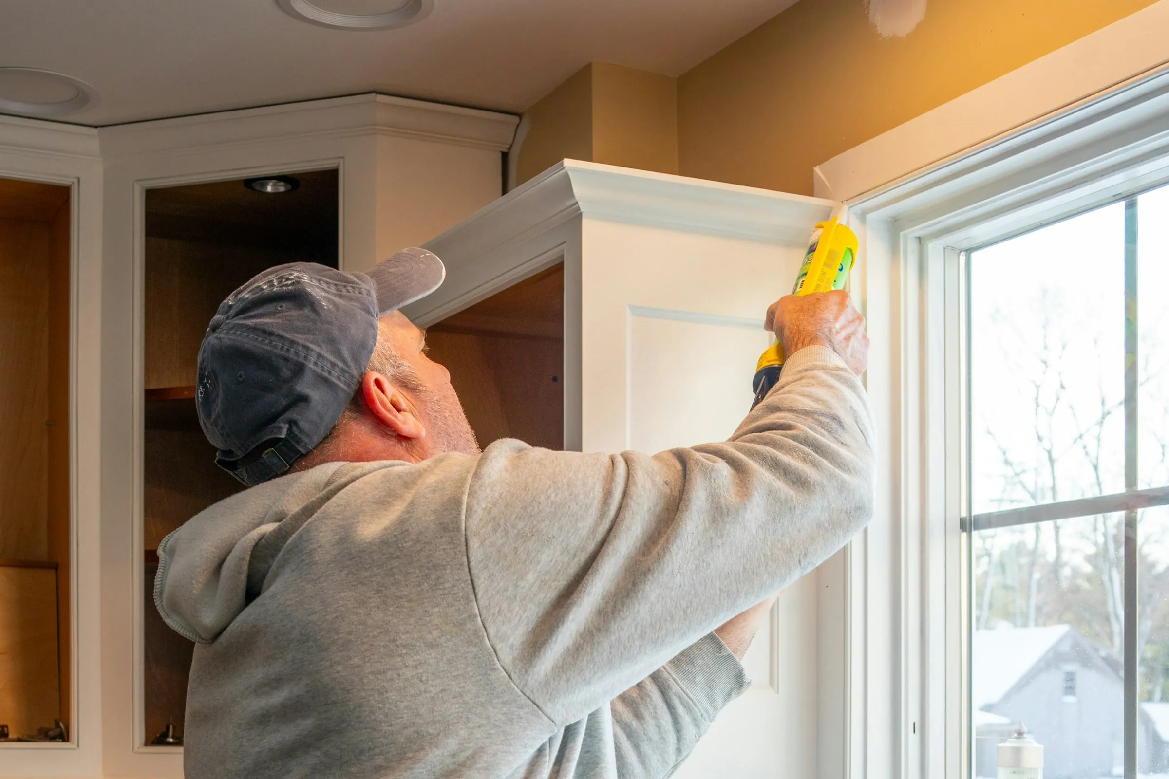 A tradesman caulking the trim beside a kitchen window